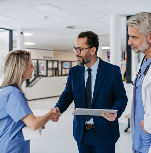 Man in suit and tablet shaking hands with surgeons